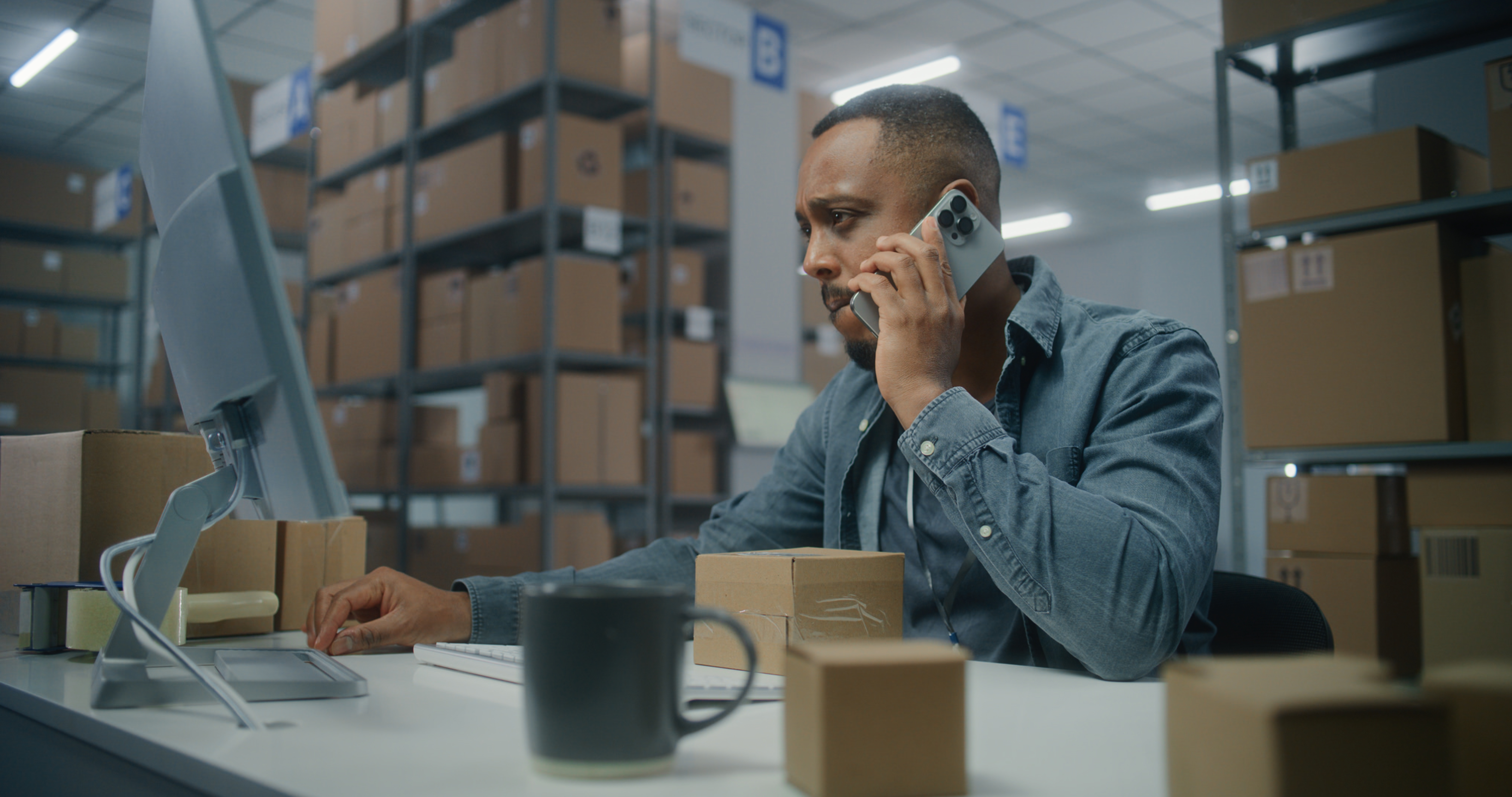 Sorting center: African American retailer or logistics manager talks to customer by mobile phone