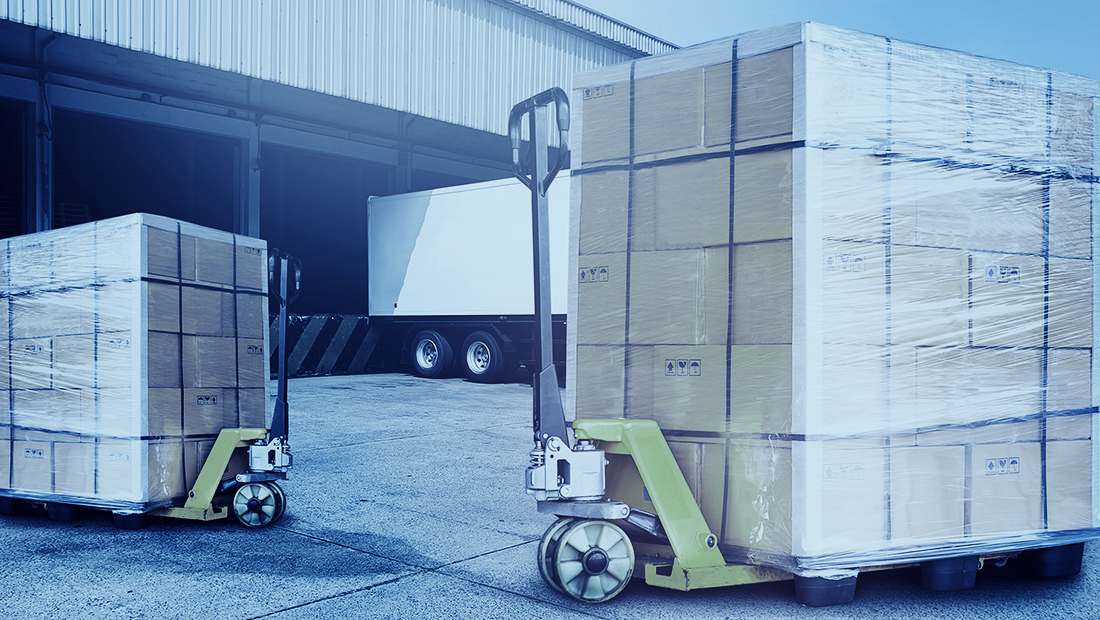 Less than truckload shipment of shrink-wrapped boxes on pallets sits in a loading dock, ready to load into a nearby semi-truck